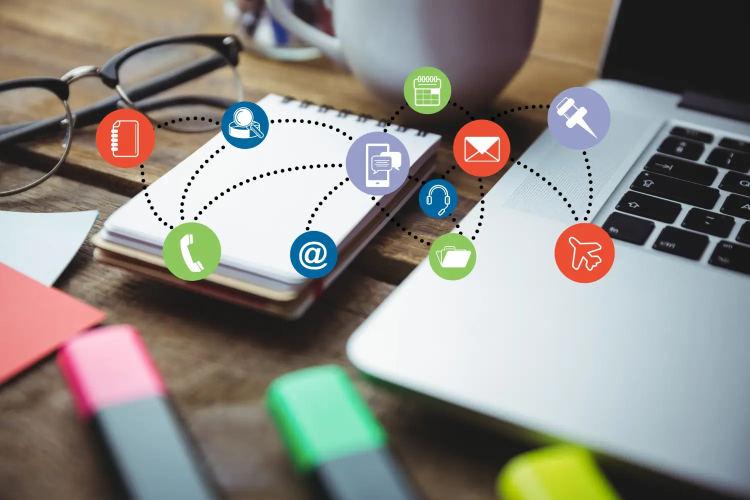 Colorful icons connecting a notebook and laptop on a desk, illustrating online marketing strategies and the power of Question Based Selling.